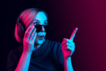 Surprised pretty woman with headphones listening to music over red neon background at studio.
