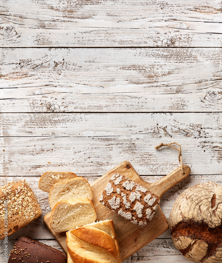 Wall mural Assortment of fresh baked bread on a wooden background. White and rye bread in a paper bag. Bakery concept with copy place