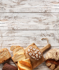Assortment of fresh baked bread on a wooden background. White and rye bread in a paper bag. Bakery...