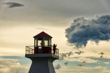 A man stood taking photos on the lighthouse at sunset in Carleton in Gaspesie, Quebec Canada