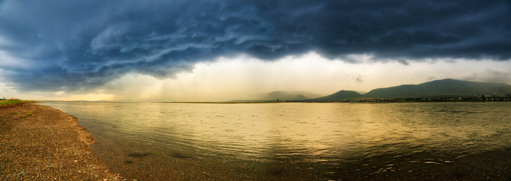 A panorama og golden evening light and a dramatic summer storm reflected in the lagoon at Carleton in Gaspesie, Quebec, Canada