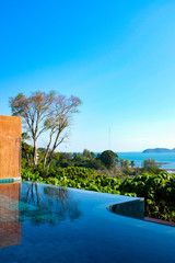 View from an infinity pool outside tropical villa resort with blue sea in background and bright blue sky