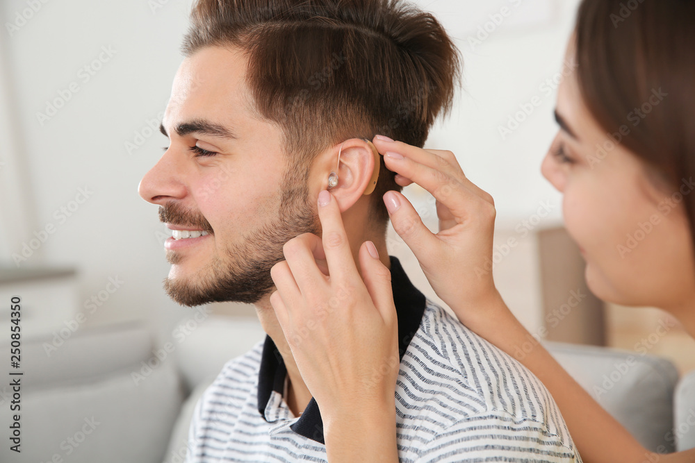 Wall mural Woman putting hearing aid in man's ear indoors