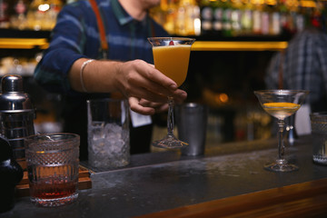 Bartender with glass of tasty cocktail at counter in nightclub, closeup