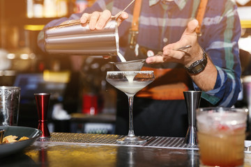 Bartender pouring tasty cocktail at counter in nightclub, closeup