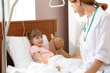Doctor visiting little child with intravenous drip in hospital