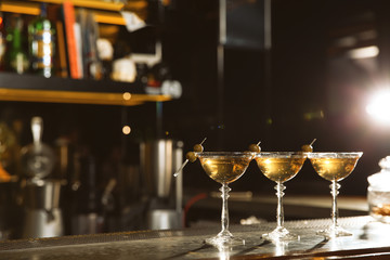 Glasses of martini cocktail with olives on bar counter. Space for text