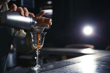 Barman pouring martini espresso cocktail into glass at counter, closeup. Space for text