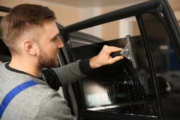 Skilled worker washing car window before tinting in shop