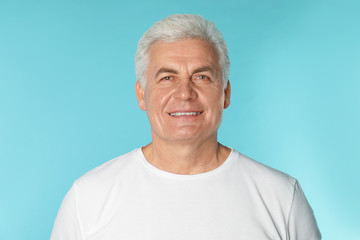 Mature man with healthy teeth on color background