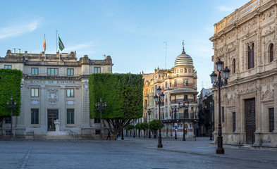 Fototapeta premium A look across the deserted cobbled Plaza de San Francisco towards the Banco de España & the lovely 'Confiteria Filella' on the 'Avenida de la Constitucion' in Seville just after sunrise.