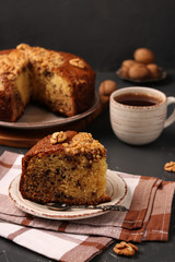 American homemade nutty cake is located on a dark background. Piece of cake in the foreground