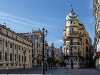 Fototapeta premium „Avenida de la Constitucion” w Sewilli tuż po wschodzie słońca, z piękną wieżą „Confiteria Filella”, „Banco de España” i katedrą
