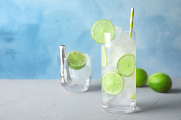 Glass of drink with lime and ice cubes on table against color background. Space for text