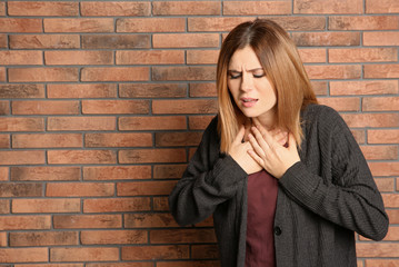 Woman suffering from cough near brick wall. Space for text