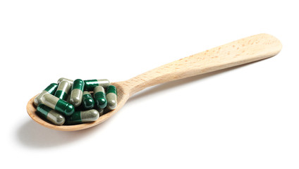 Wooden spoon with green spirulina capsules on white background