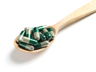 Wooden spoon with green spirulina capsules on white background