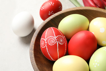 Fototapeta na wymiar Bowl with painted Easter eggs on light background, closeup