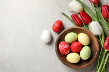 Flat lay composition of painted Easter eggs and spring flowers on light background, space for text