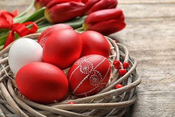 Wicker nest with painted Easter eggs on table, closeup