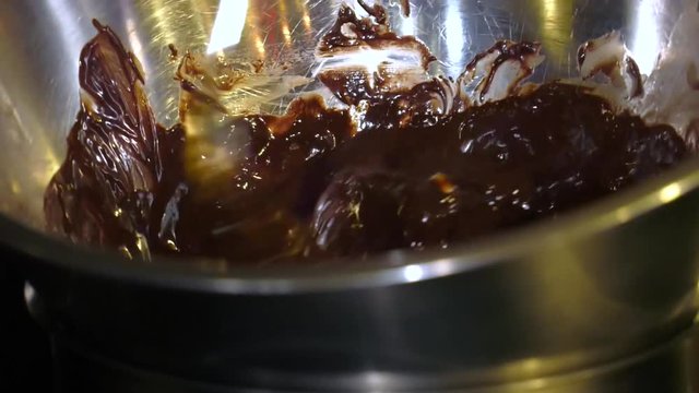 Chocolate Fondant. Close-up of a cook stirring a melting mixture of chocolate and butter. Cooking dessert. Melt chocolate in a water bath. Cook mixes chocolate and butter with a spoon. Slow motion sti