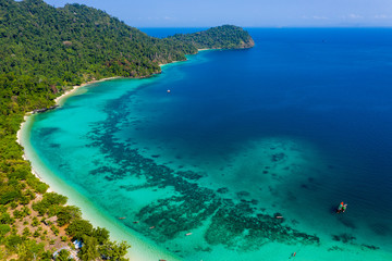 Fototapeta na wymiar Aerial drone view of a beautiful tropical island surrounded by coral reefs and covered with lush, green jungle (Kyun Phi Lar, Myanmar)