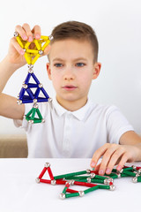 Close-up of child playing board game with magnetic sticks and balls while sitting at the table at home. Development, fine motor skills and creativity concept
