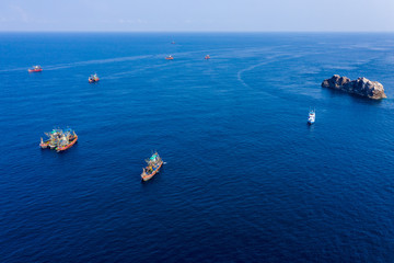 Aerial drone view of a fleet of large fishing trawlers surrounding a single SCUBA diving boat at the Black Rock dive site in the Mergui Archipelago, Myanmar