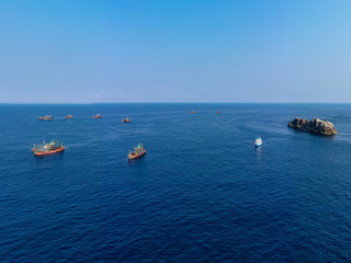 Aerial drone view of a fleet of large fishing trawlers surrounding a single SCUBA diving boat at the Black Rock dive site in the Mergui Archipelago, Myanmar
