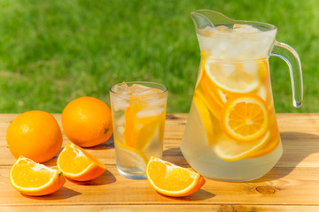 homemade lemonade from oranges on a wooden table on a background of green grass