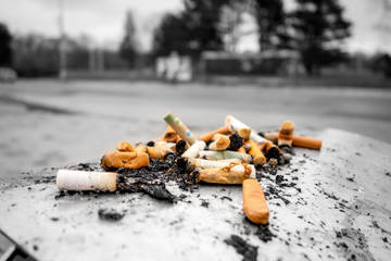 Lots of cigarette butts on an ashtray of a dustbin making an annoying smell around