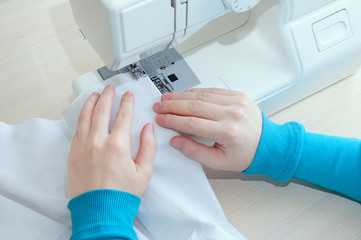 Obraz na płótnie Canvas Caucasian girl sews cotton white fabric on the sewing machine. Close-up.