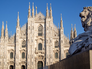Detail of lion statue and Duomo di Milano (Milan Cathedral) in the background in the sunny evening.