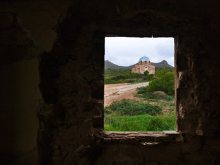 Old orthodox church  under sky with clouds framed by a window in a ruined house, in Attica,  Greece