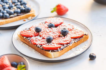 Close-up of breakfast sweet toast with chocolate spread, strawberry slices, blueberry and coconut chips.