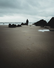 woman standing on beach looking to sea with rocks