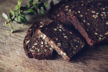 Close-up of the sliced brown bread at the cutting board on the wooden table with black background. Detailed close-up shot