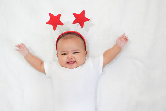 Asian newborn baby is wearing red stars headband on white background.