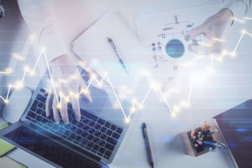 Hands typing on laptop. Business and Financial concept. Double exposure of stock market charts.