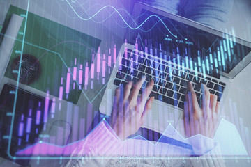 Hands typing on laptop. Business and Financial concept. Double exposure of stock market charts.