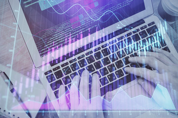 Hands typing on laptop. Business and Financial concept. Double exposure of stock market charts.