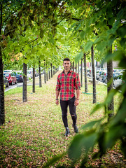 One handsome young man in urban setting in modern European city, wearing jeans and red checkered shirt