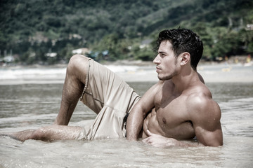 Handsome young man laying down on a beach in Phuket Island, Thailand, shirtless wearing boxer shorts, showing muscular fit body