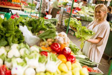 Cute young woman buying vegetables at the market