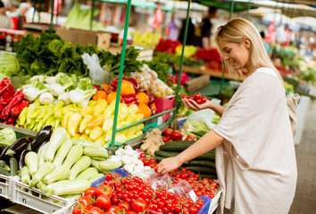 Cute young woman buying vegetables at the market