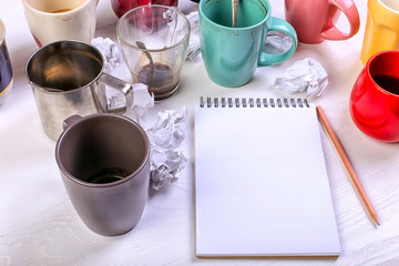 Empty dirty coffee cups, different colors on the table and a notebook for writing a letter. Concept caffeine dope, lack of energy to solve the problem. Copy space.