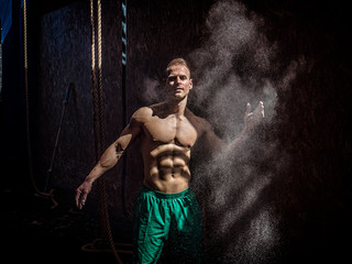 Shirtless man using chalk or magnesium powder in gym, clapping hands and creating cloud
