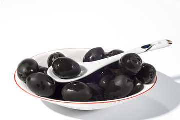 Black olives in a white plate on a white background close up. A dish on a table