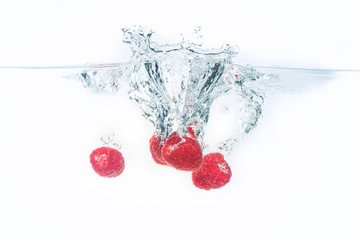 Bunch of raspberries splashing into water surface and sinking. Isolated on white background, splash food photography.