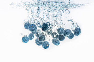 Bunch of blueberries splashing into water surface and sinking. Isolated on white background, splash food photography.